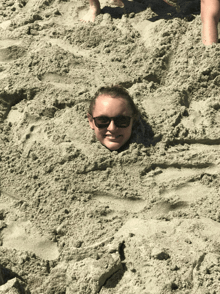 a woman is buried in sand with her head sticking out