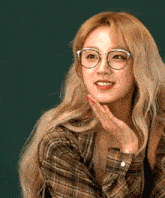 a woman wearing glasses and a plaid shirt is holding her hand to her chin .