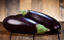 two purple eggplant on a wooden table with a green stem