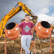 a boy wearing a t-shirt that says classic stands in front of a yellow tab construct excavator