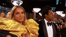 a woman in a gold dress and a man in a tuxedo are sitting next to each other at a awards show .