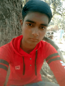 a young man wearing a red shirt with a white square on the sleeve that says ' reebok '