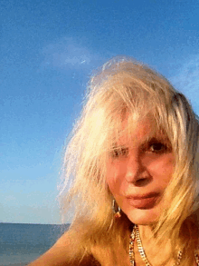 a woman with blonde hair looks at the camera with a blue sky behind her