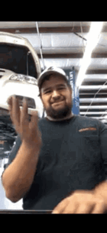 a man with a beard is standing in front of a car in a garage holding a piece of metal .