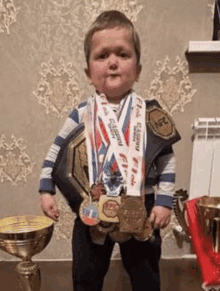 a young boy is holding a trophy and medals while wearing a wrestling belt .