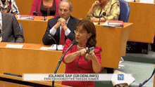 a woman in a red dress is speaking into a microphone in front of a sign that says jolande sap groenlinks