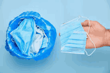 a person is holding a surgical mask next to a trash can full of surgical masks .