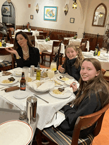 a woman and two girls are sitting at a table with a bottle of cerveza