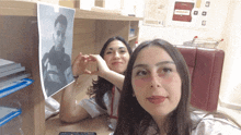 two women making a heart shape with their hands in front of a fire alarm