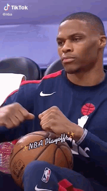 a man is sitting in a chair with a basketball in his lap and a nba logo on his shirt .