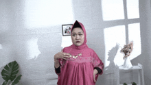 a woman wearing a pink dress and a hijab is standing in front of a window .