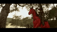 a man is riding on the back of a red horse in a field .