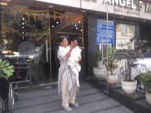 a woman is holding a baby in front of a building that says angel 's inn