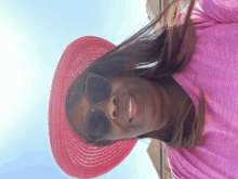 a woman wearing sunglasses and a pink hat is smiling