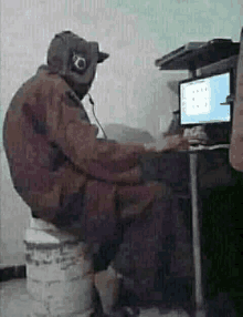 a man is sitting on a bucket in front of a computer monitor .