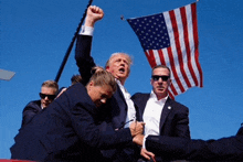 a man in a suit holds up his fist in the air while a woman tries to stop him