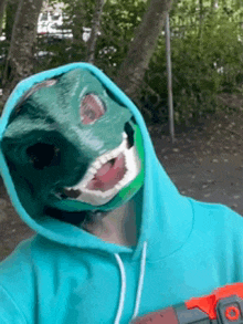 a person wearing a blue hoodie and a green mask is holding a toy gun