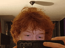 a person with red hair is taking a selfie with a cell phone