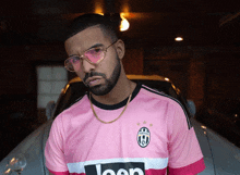 a man wearing a pink jeep jersey stands in front of a car