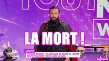 a man with a beard is standing in front of a sign that says " la mort "