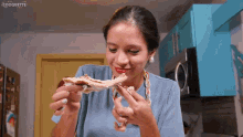 a woman in a blue shirt is eating a piece of meat in a kitchen with a coquette logo in the corner