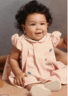 a baby girl wearing a pink dress and white shoes is smiling