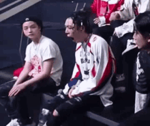 a group of young men are sitting in a stadium . one of the men is wearing a hat .