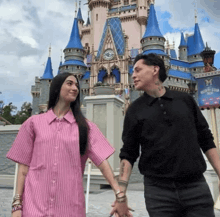 a man and a woman are holding hands in front of a castle