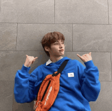 a young man wearing a blue sweatshirt and an orange bag with the word supreme on it