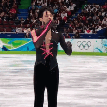 a man in a black and pink outfit is standing on a ice rink with the olympic rings in the background