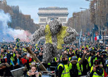 a crowd of people are gathered on a street with a large statue in the background