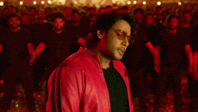 a man wearing sunglasses and a red jacket is standing in front of a crowd of people