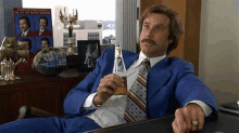 a man in a suit and tie is sitting at a desk drinking a beer .