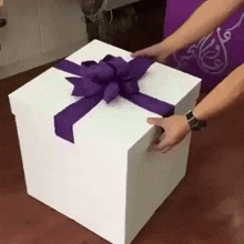 a person is opening a large white gift box with a purple bow .