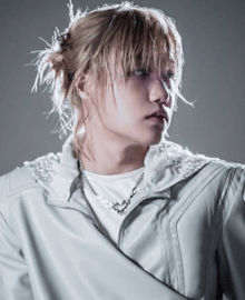 a woman with blonde hair is wearing a white jacket and a silver chain around her neck