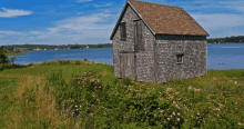 a small house sits in the middle of a grassy field near a body of water