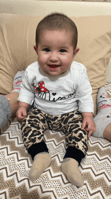 a baby wearing a minnie mouse shirt and leopard print pants is sitting on a bed