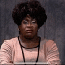 a woman with curly hair is sitting at a table with her arms crossed and looking at the camera .