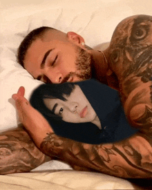 a man with a tattoo on his arm is sleeping with a picture of another man on his pillow