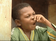 a young boy in a green and yellow shirt is covering his nose