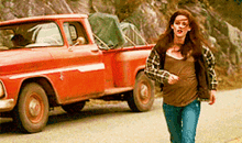 a woman in a plaid shirt is running down a road next to a red truck .