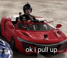 a man is driving a red sports car with the words `` ok i pull up '' written on the bottom .