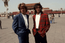 a man in a plaid jacket is standing next to another man in a blue suit