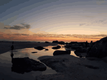 a sunset over a rocky beach with people standing on the rocks