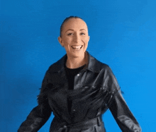 a woman in a black leather jacket is smiling and dancing against a blue background .