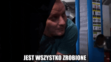 a man in a green shirt is standing in front of a machine that says jest wszystko zrobione on it