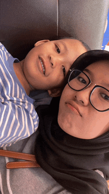 a woman wearing glasses and a hijab is holding a child