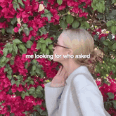 a woman stands in front of a bush with pink flowers and the words " me looking for who asked "