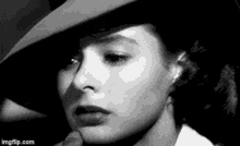 a woman wearing a hat and a white shirt is looking at the camera in a black and white photo .