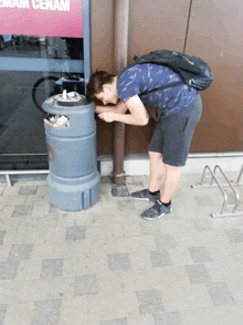 a man with a backpack looks into a trash can in front of a sign that says emam cenam